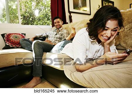 Couple using cell phones on sofa in living room View Large Photo Image Stock Photography - Couple using cell phones on sofa in living room. Fotosearch