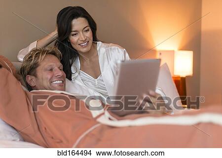 Picture - Couple using digital tablet on bed. Fotosearch