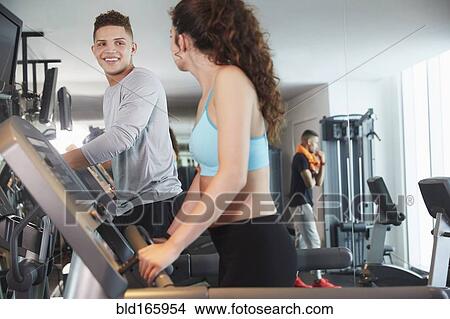 Picture - Couple using exercise machines in gym. Fotosearch