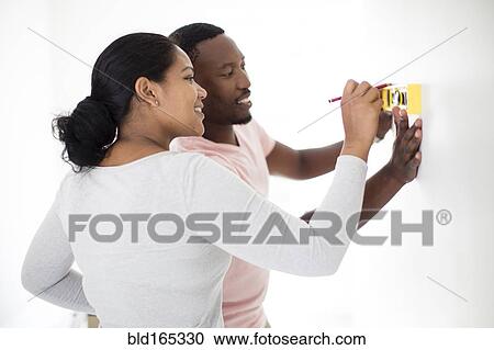 Stock Image - Couple using level in new home. Fotosearch