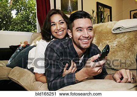 Stock Image - Couple watching television on sofa in living room. Fotosearch