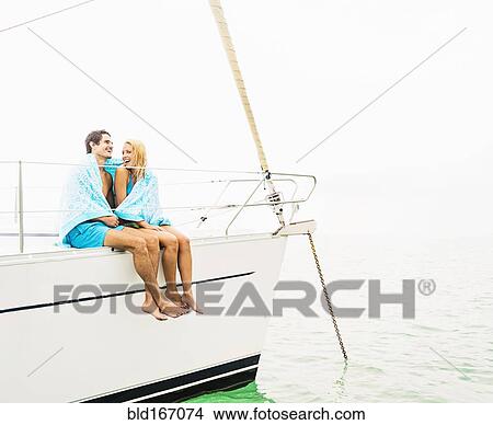 Picture - Couple wrapped in towels on deck of sailboat. Fotosearch