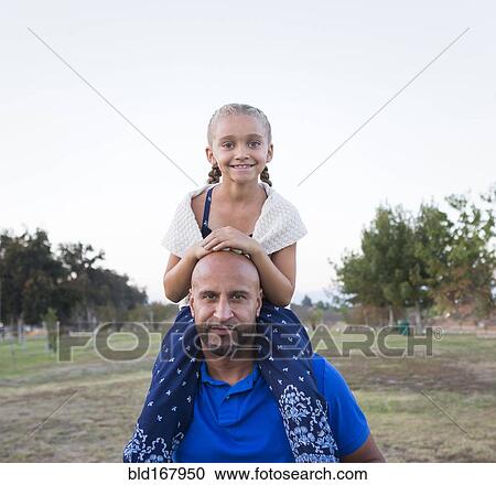 Stock Image - Father carrying daughter on shoulders in park. Fotosearch
