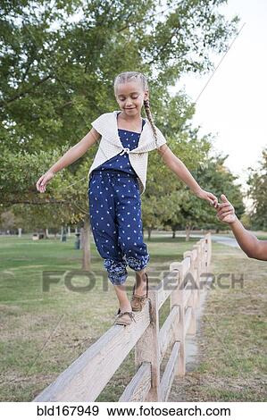 Stock Photo - Father helping daughter balance on wooden fence. Fotosearch