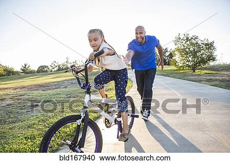 Father teaching daughter to ride bicycle in park View Large Photo Image Stock Image - Father teaching daughter to ride bicycle in park. Fotosearch