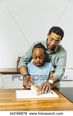 Father teaching daughter to slice bread in kitchen View Large Photo Image Stock Photo - Father teaching daughter to slice bread in kitchen. Fotosearch