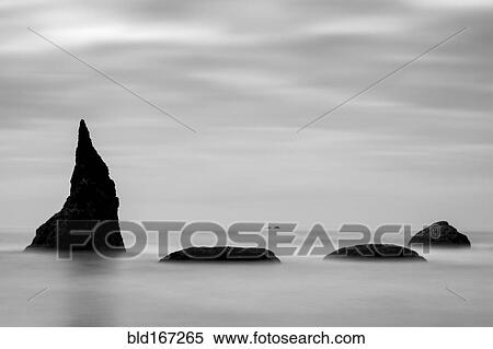 Stock Photography - Fog over rock formations in ocean under cloudy sky. Fotosearch