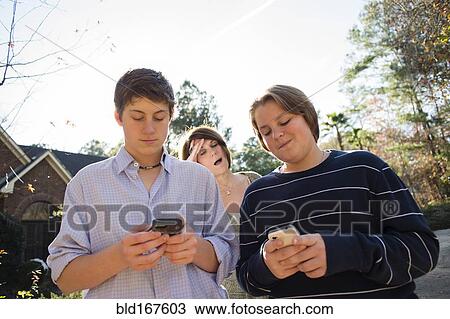 Stock Image - Frustrated Caucasian mother watching sons use cell phones. Fotosearch