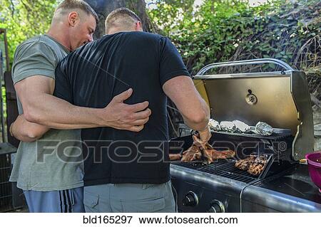 Stock Photo - Gay couple grilling food in backyard. Fotosearch