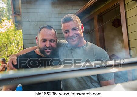 Stock Photograph - Gay couple grilling food in backyard. Fotosearch