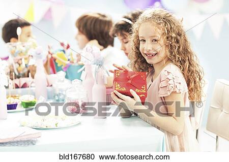 Stock Image - Girl holding wrapped gift at birthday party. Fotosearch