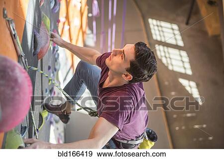 Stock Photo - High angle view of athlete climbing rock wall in gym. Fotosearch