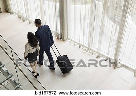 Stock Image - High angle view of business people rolling luggage in hotel lobby. Fotosearch