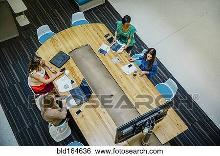 Stock Photograph - High angle view of businesswomen working in office meeting. Fotosearch