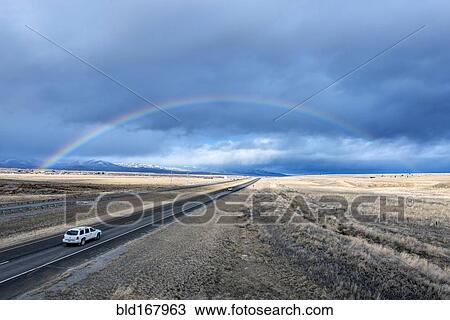 Stock Image - High angle view of car driving to rainbow on remote road. Fotosearch