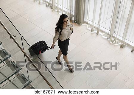 Stock Image - High angle view of mixed race businesswoman rolling luggage in hotel lobby. Fotosearch