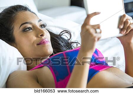 Stock Image - Hispanic athlete using digital tablet on bed. Fotosearch