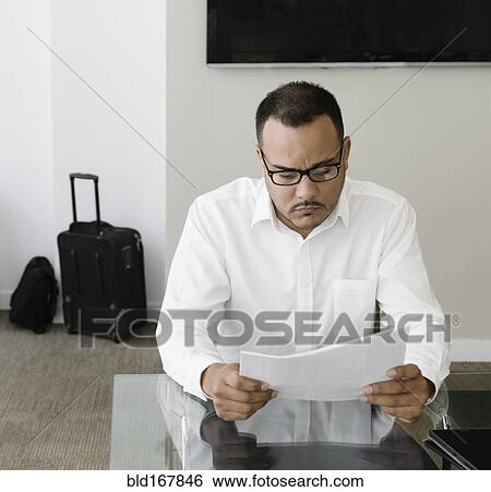 Stock Photograph - Hispanic businessman reading paperwork in office. Fotosearch