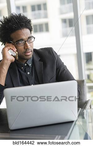 Stock Image - Hispanic businessman talking on cell phone in office. Fotosearch