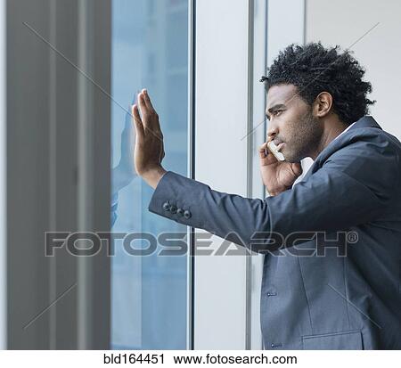 Stock Image - Hispanic businessman talking on cell phone at office window. Fotosearch