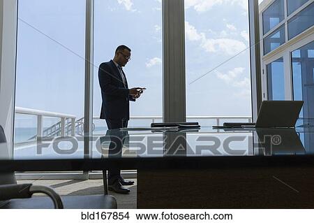 Picture - Hispanic businessman using cell phone in conference room. Fotosearch