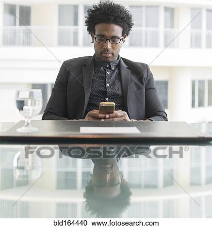 Stock Image - Hispanic businessman using cell phone at conference table. Fotosearch