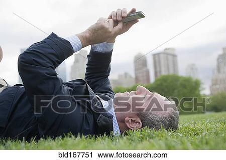 Stock Image - Hispanic businessman using cell phone in urban park, New York, New York, United States. Fotosearch