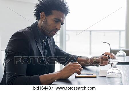 Stock Photo - Hispanic businessman using cell phone at conference table. Fotosearch