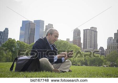 Stock Photo - Hispanic businessman using cell phone in urban park, New York, New York, United States. Fotosearch