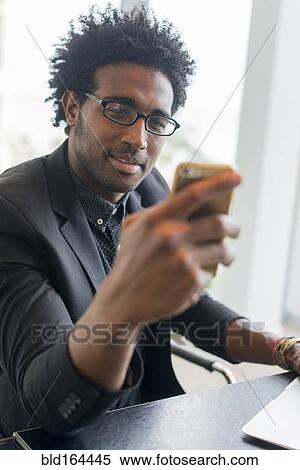 Stock Photography - Hispanic businessman using cell phone in office. Fotosearch