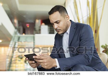 Stock Image - Hispanic businessman using digital tablet in hotel lobby. Fotosearch