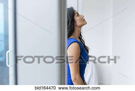 Stock Image - Hispanic businesswoman standing at office window. Fotosearch