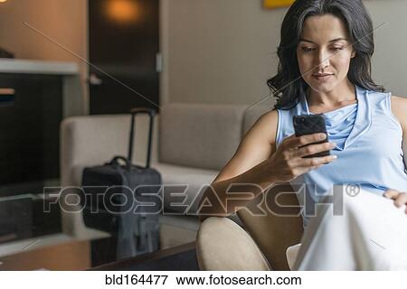 Stock Photo - Hispanic businesswoman using cell phone in office lobby. Fotosearch
