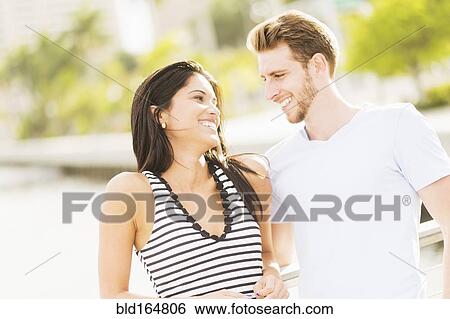 Stock Photograph - Hispanic couple hugging on bridge over urban river. Fotosearch