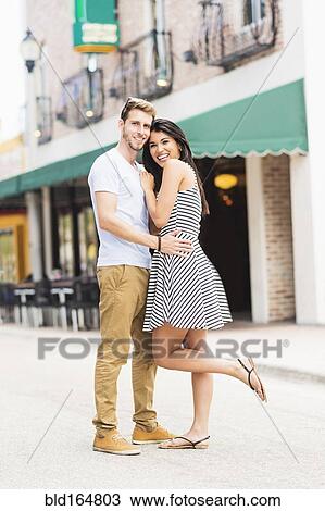 Stock Image - Hispanic couple hugging on sidewalk. Fotosearch