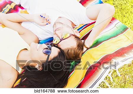 Stock Photo - Hispanic couple laying on blanket in park. Fotosearch