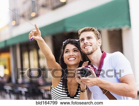 Stock Photo - Hispanic couple photographing on city sidewalk. Fotosearch