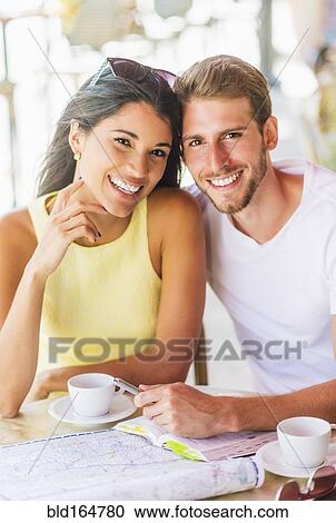 Stock Image - Hispanic couple reading map at cafe. Fotosearch