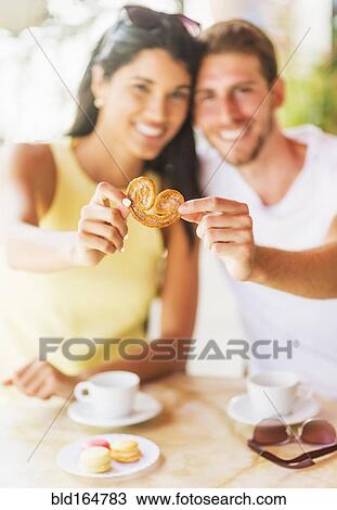 Stock Image - Hispanic couple sharing cookie at cafe. Fotosearch
