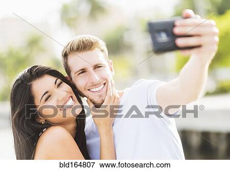 Stock Photo - Hispanic couple taking selfie outdoors. Fotosearch