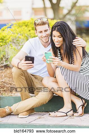 Stock Image - Hispanic couple using cell phones on sidewalk. Fotosearch