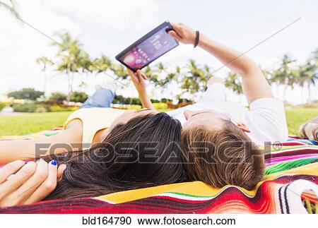 Stock Image - Hispanic couple using digital tablet on blanket in park. Fotosearch