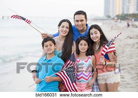 Stock Image - Hispanic family waving American flags on beach. Fotosearch