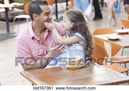 Stock Image - Hispanic father and daughter eating at sidewalk cafe. Fotosearch
