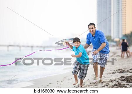 Stock Image - Hispanic father and son flying kite on beach. Fotosearch