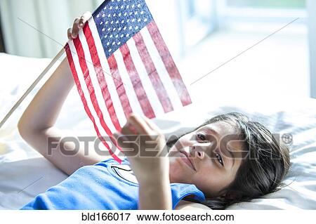Hispanic girl holding American flag on bed View Large Photo Image Stock Photo - Hispanic girl holding American flag on bed. Fotosearch
