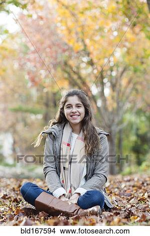 Picture - Hispanic girl sitting in autumn leaves. Fotosearch