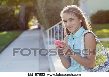Stock Image - Hispanic girl using cell phone on sidewalk. Fotosearch