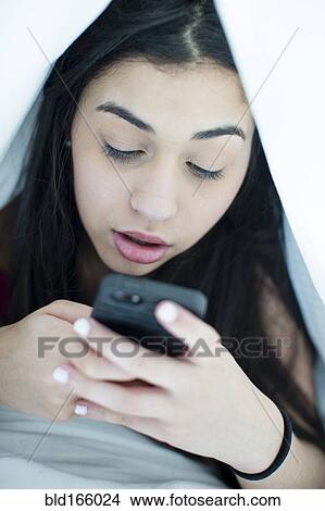 Hispanic girl using cell phone under blanket View Large Photo Image Picture - Hispanic girl using cell phone under blanket. Fotosearch