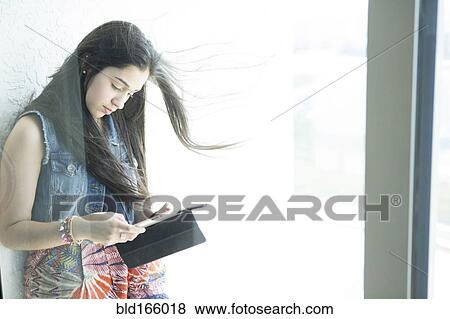 Stock Photo - Hispanic girl using digital tablet at window. Fotosearch